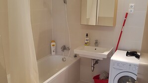 Een badkamer met een bad, een wastafel, een spiegel, een wasmachine en een toilet.