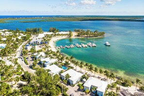 An aerial view of a coastal resort with multiple buildings, a marina with boats, and a clear view of the ocean.