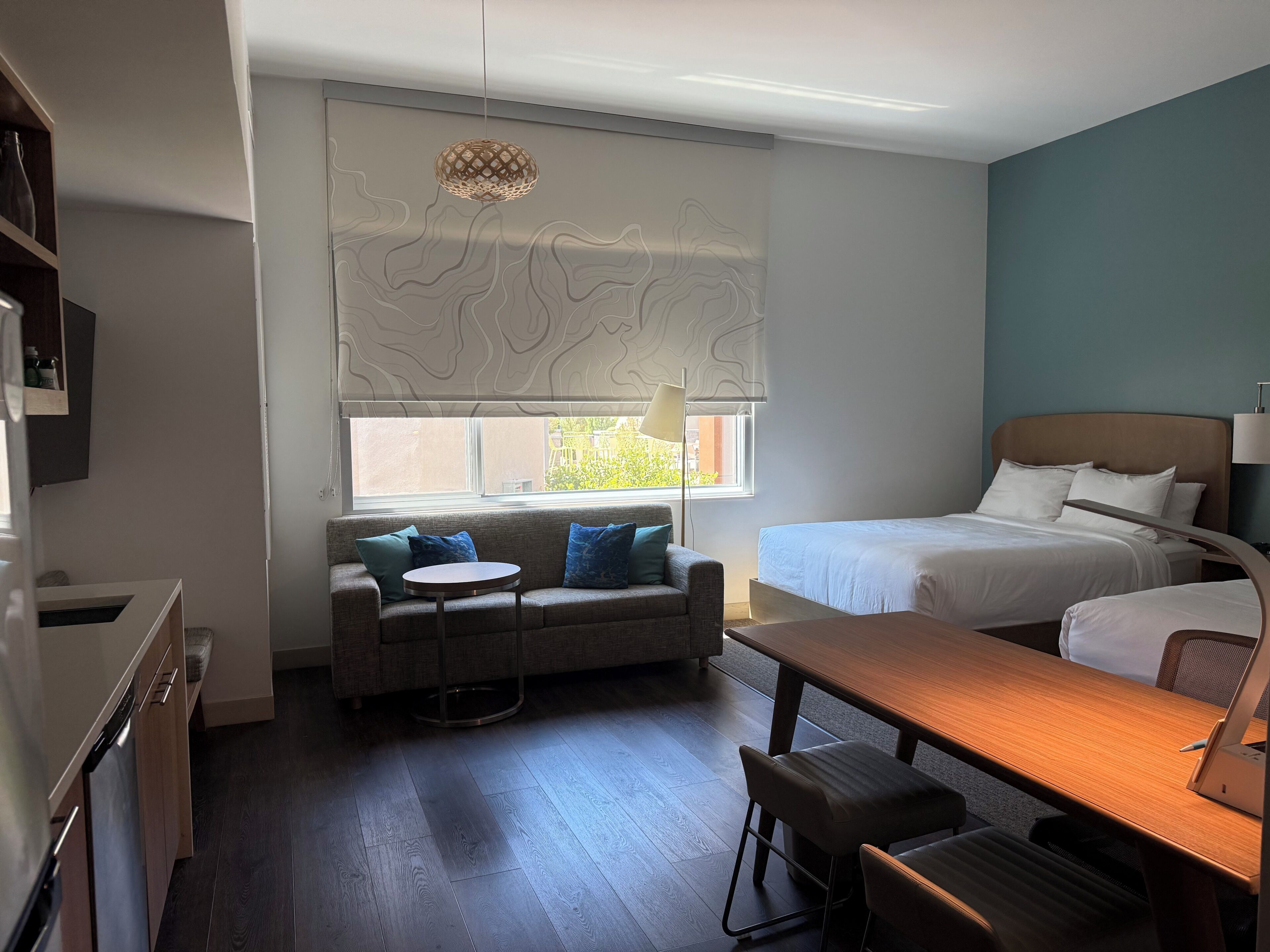 Una habitación de hotel moderna con cama, sofá, una pequeña mesa de comedor y ventana con vistas.