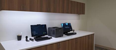 Un espacio de trabajo con dos monitores de ordenador, una impresora y un teclado sobre un escritorio blanco, con armarios de madera arriba.