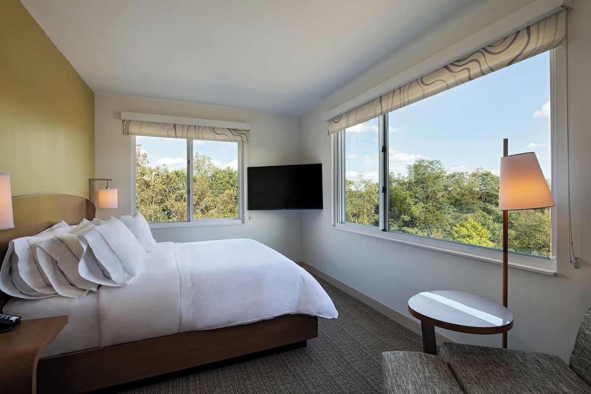 A hotel room with a large bed, a flat-screen TV mounted on the wall, a small round table, and a lamp.
