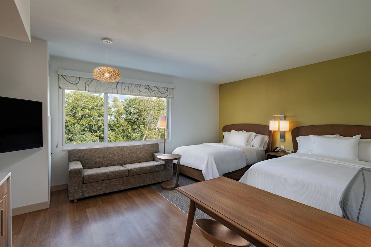 A hotel room with a sofa, two beds, a TV, and a dining table.