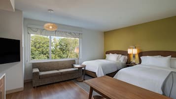 Habitación de hotel con sofá, dos camas, televisor y mesa de comedor.