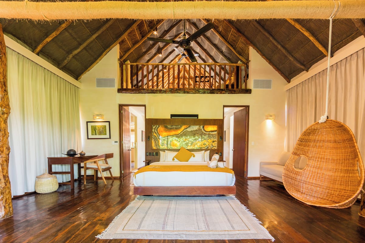 A bedroom with a bed, a desk, a chair, a hanging chair, and a painting on the wall.
