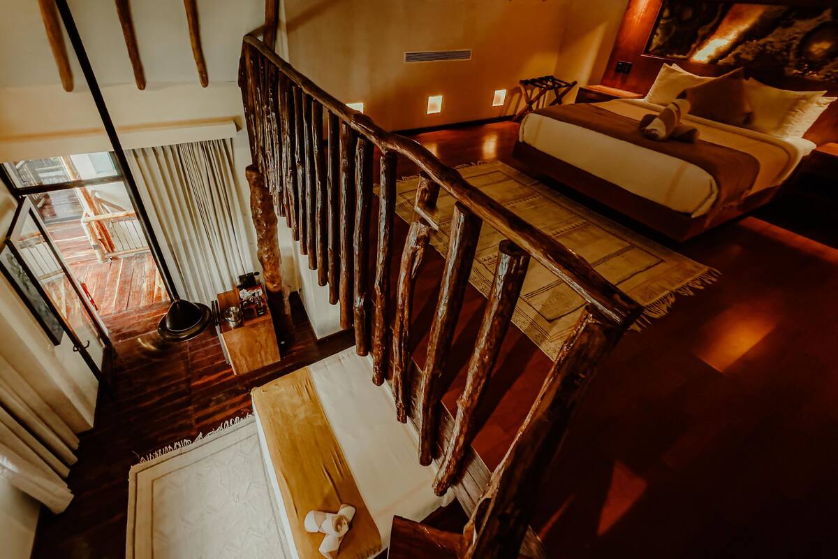 A high-ceilinged room with a wooden staircase, a sofa, and a view of the outdoors.