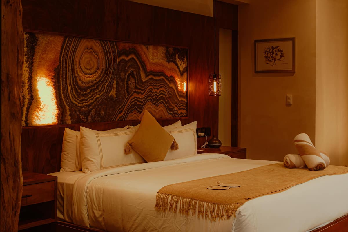 A bedroom with a large bed, a headboard with a marbled design, a bedside table with a lamp, and a wall-mounted artwork.