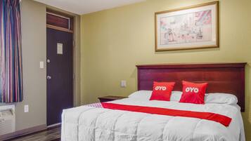 A hotel room with a large bed, two red pillows with "OYO" branding, a framed cityscape picture on the wall, and a door with a striped curtain.