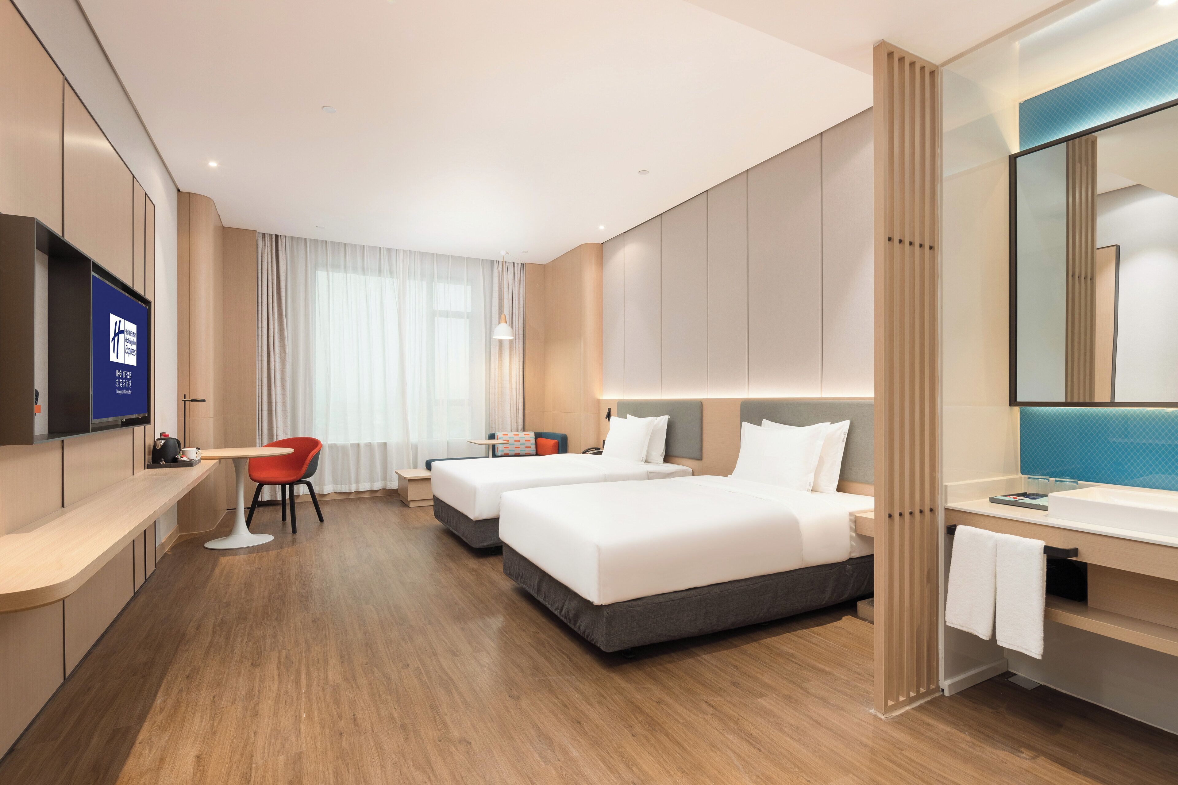 Habitación de hotel con dos camas, un escritorio, una silla, un televisor y un baño con espejo.