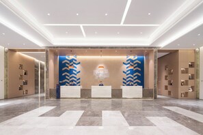 Een hotel receptie met een modern ontwerp, met een marmeren vloer, een receptiebalie en een muur met een geometrisch patroon.