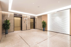 A modern elevator area with marble flooring, two elevators, and potted plants. - Holiday inn Express Dongguan Shatian by IHG (Dongguan)