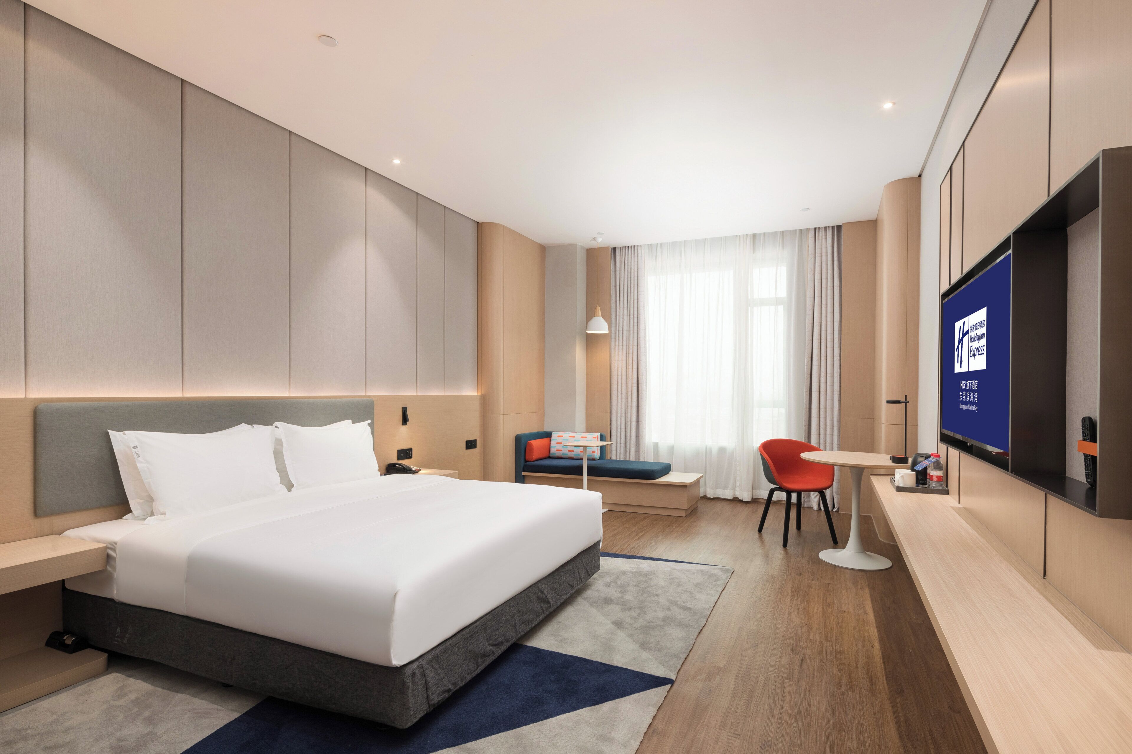 A modern hotel room with a large bed, a desk, a chair, and a television.