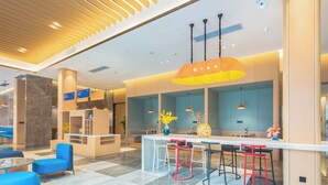 Een moderne hotellobby met een receptiebalie, een zithoek en een bar met krukken.