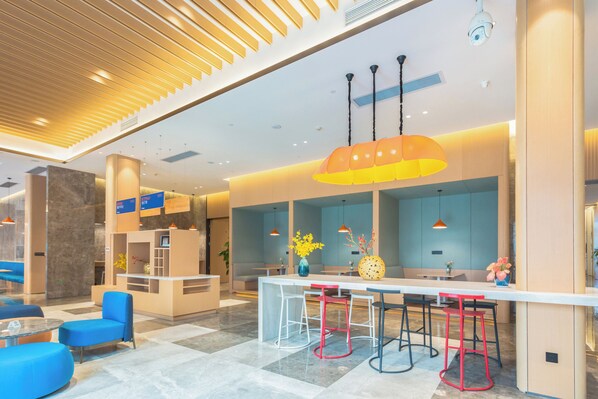 A modern hotel lobby with a reception desk, seating area, and a bar with stools.