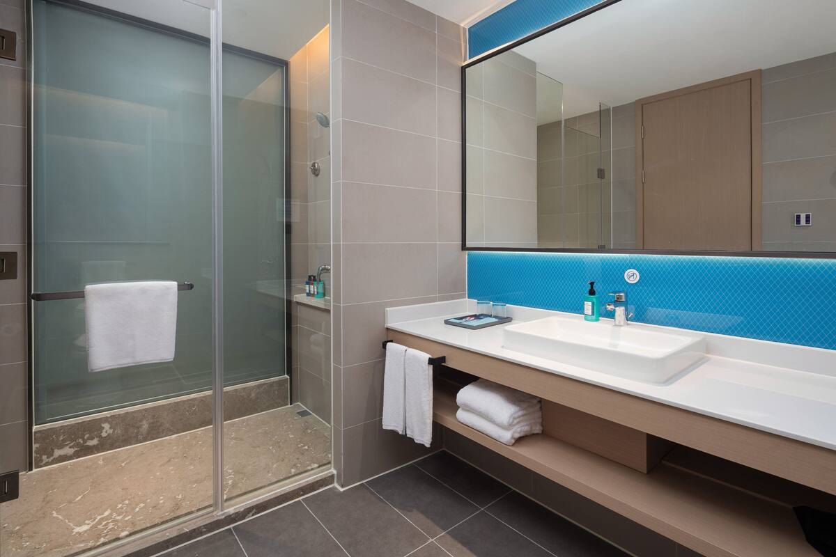 Un bany modern amb un box de dutxa de vidre, un lavabo blanc i una paret d'accent blau, i un mirall gran.
