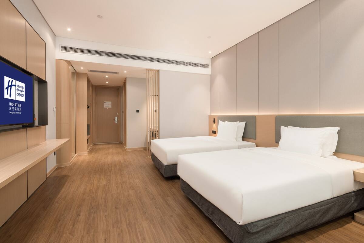 Habitació d'hotel amb dos llits, un televisor penjat a la paret i un terra de fusta.
