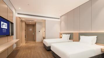 A hotel room with two beds, a TV on the wall, and a wooden floor.