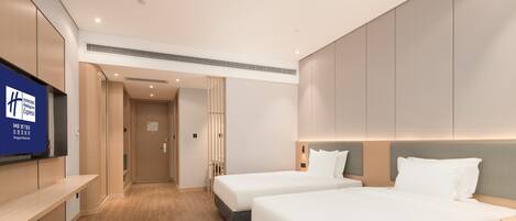 A hotel room with two beds, a TV on the wall, and a wooden floor.