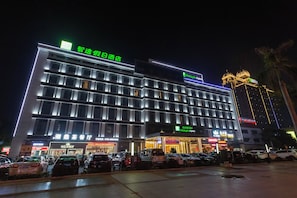 Ein Hotel mit mehreren Etagen, beleuchteter Beschilderung und einem Parkplatz mit einigen Autos.