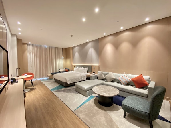 A modern hotel room with a large bed, a sofa, a coffee table, and a desk with a chair. - Holiday inn Express Dongguan Shatian by IHG (Dongguan)