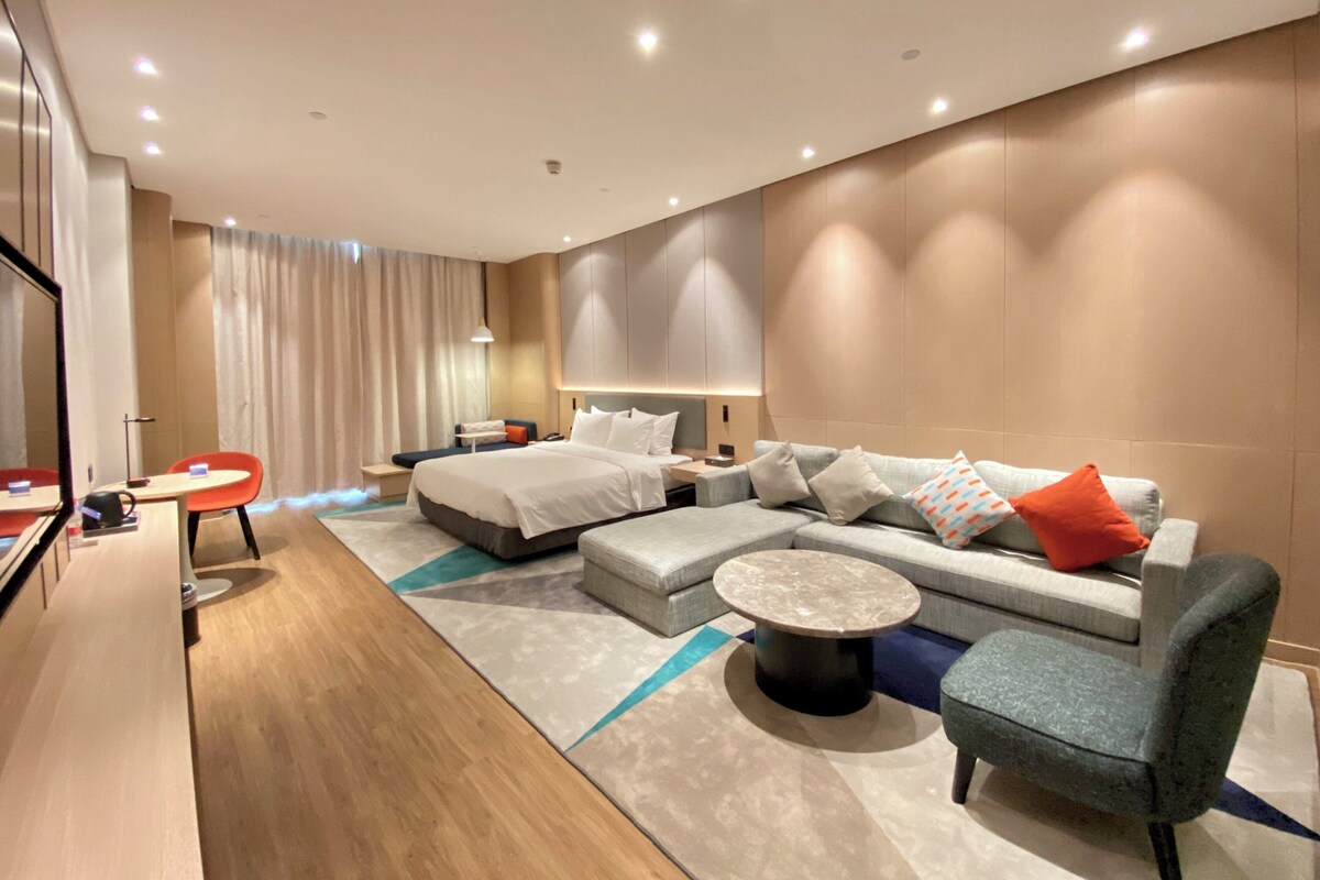 A modern hotel room with a large bed, a sofa, a small table, and a chair.