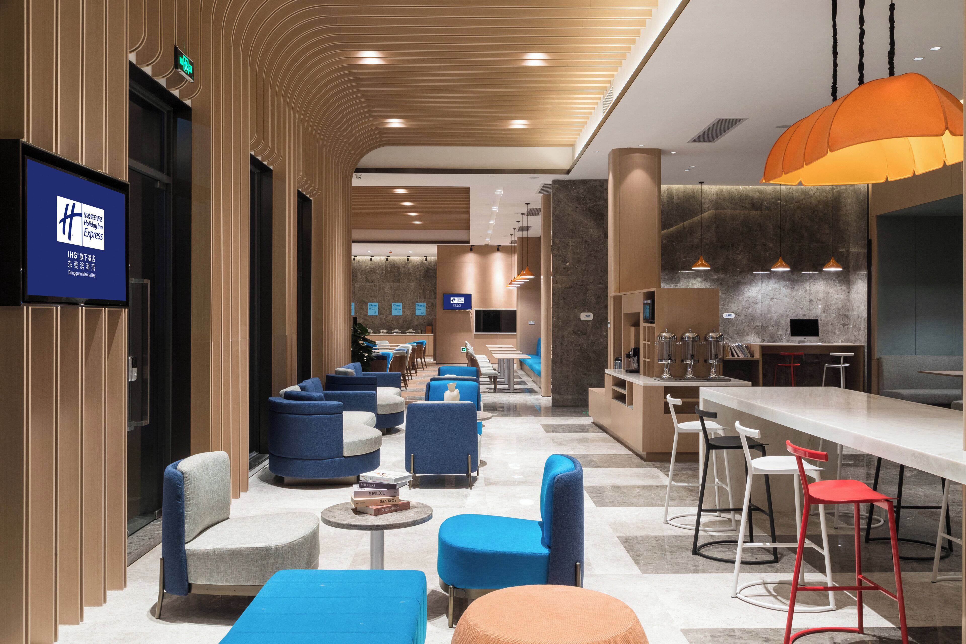 Un vestíbulo de hotel con zonas de estar, un mostrador de recepción y un bar/lounge con decoración moderna.