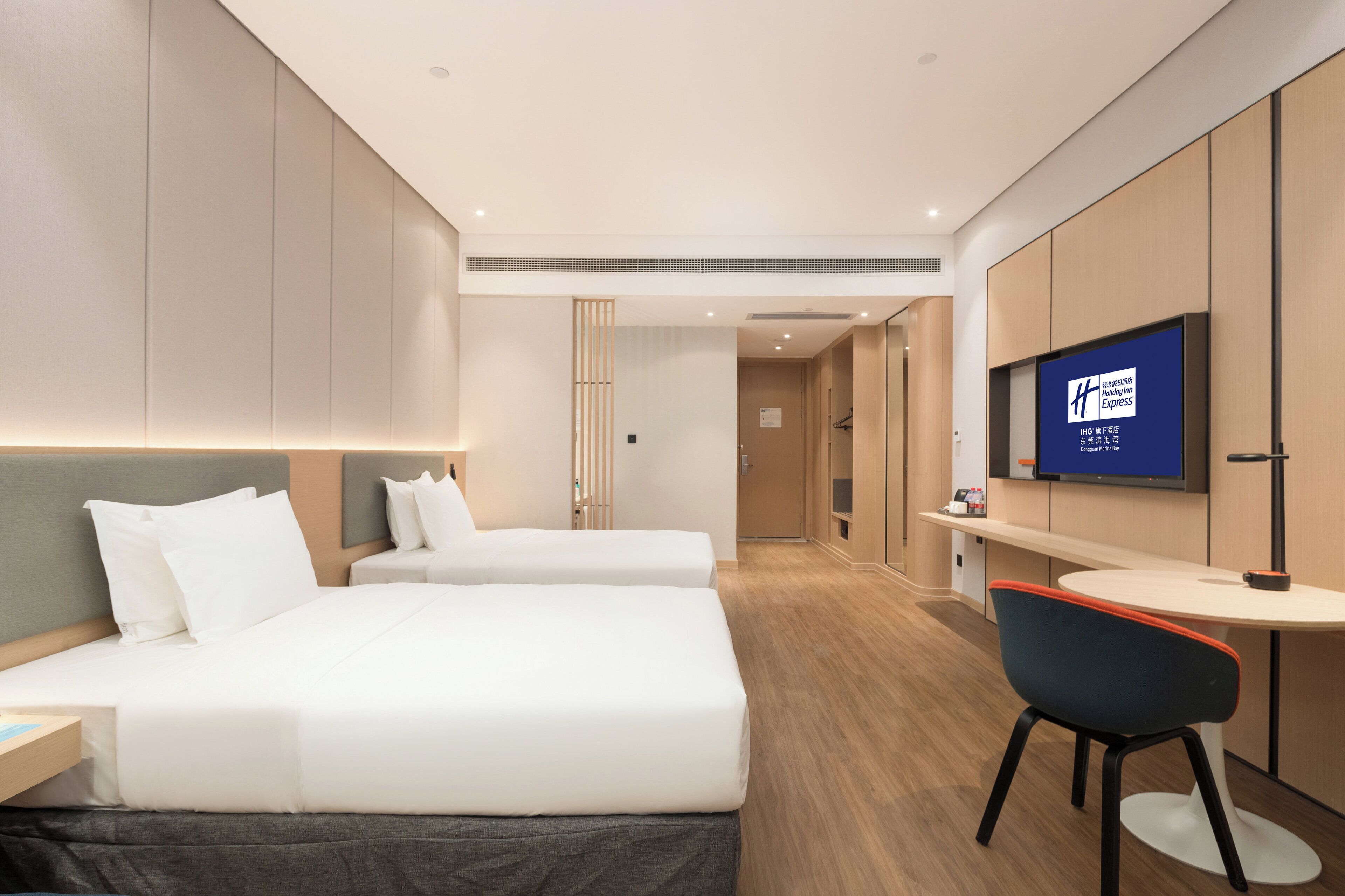 A hotel room with two beds, a desk, a chair, a TV, and a minibar.