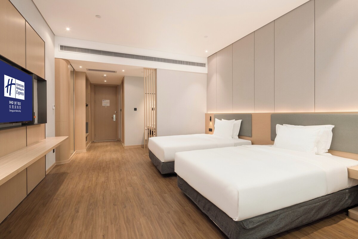 A hotel room with two beds, a TV, and a wooden floor.