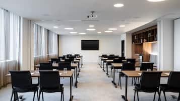 A conference room with rows of tables and chairs, a projector, and a large screen on the wall.