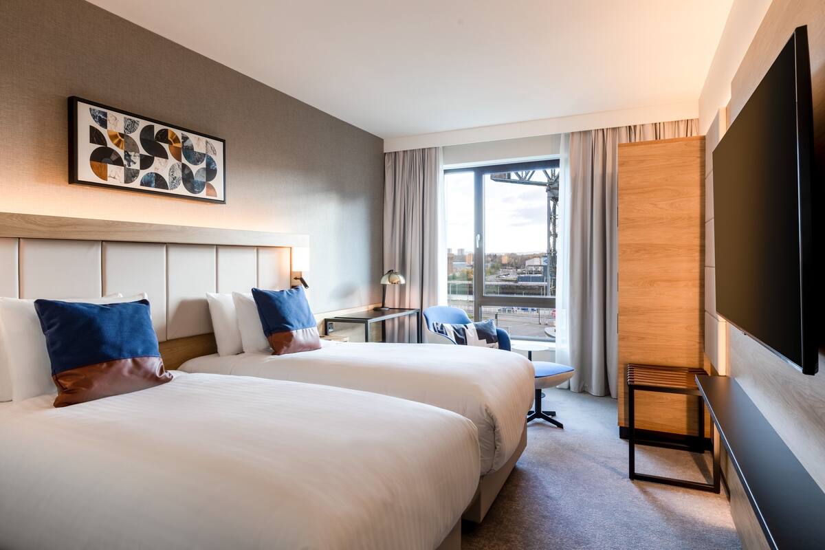 Habitación de hotel con dos camas, televisión, escritorio y vistas a la ciudad.