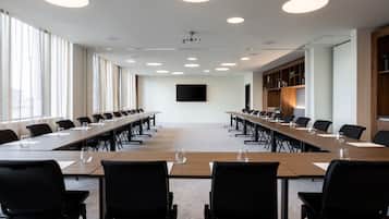 A conference room with long tables, black chairs, and a large screen on the wall.