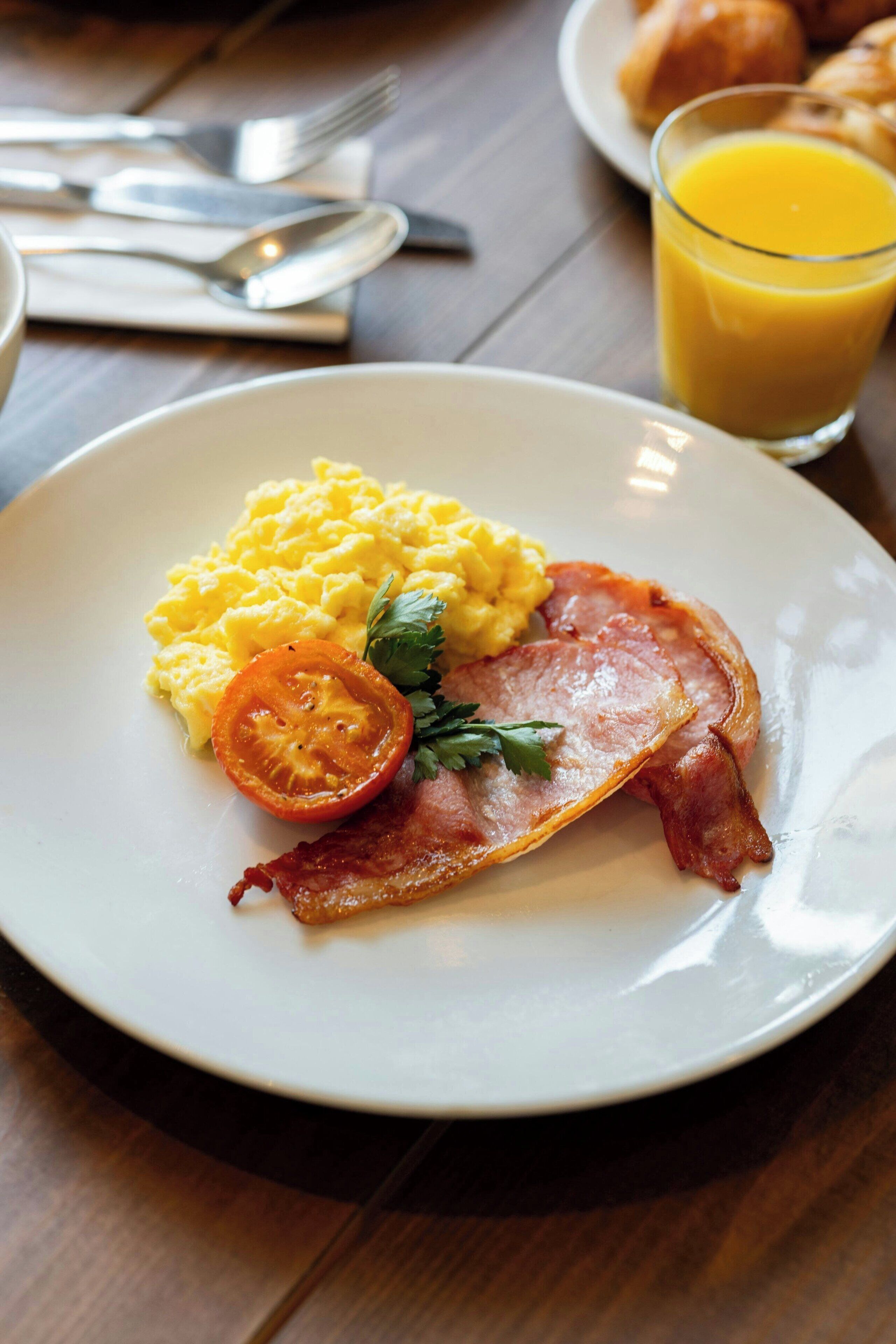 A plate with scrambled eggs, bacon, and a tomato slice on a white plate.