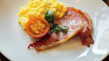 Ein Teller mit Rührei, Speck und einer Tomatenscheibe.