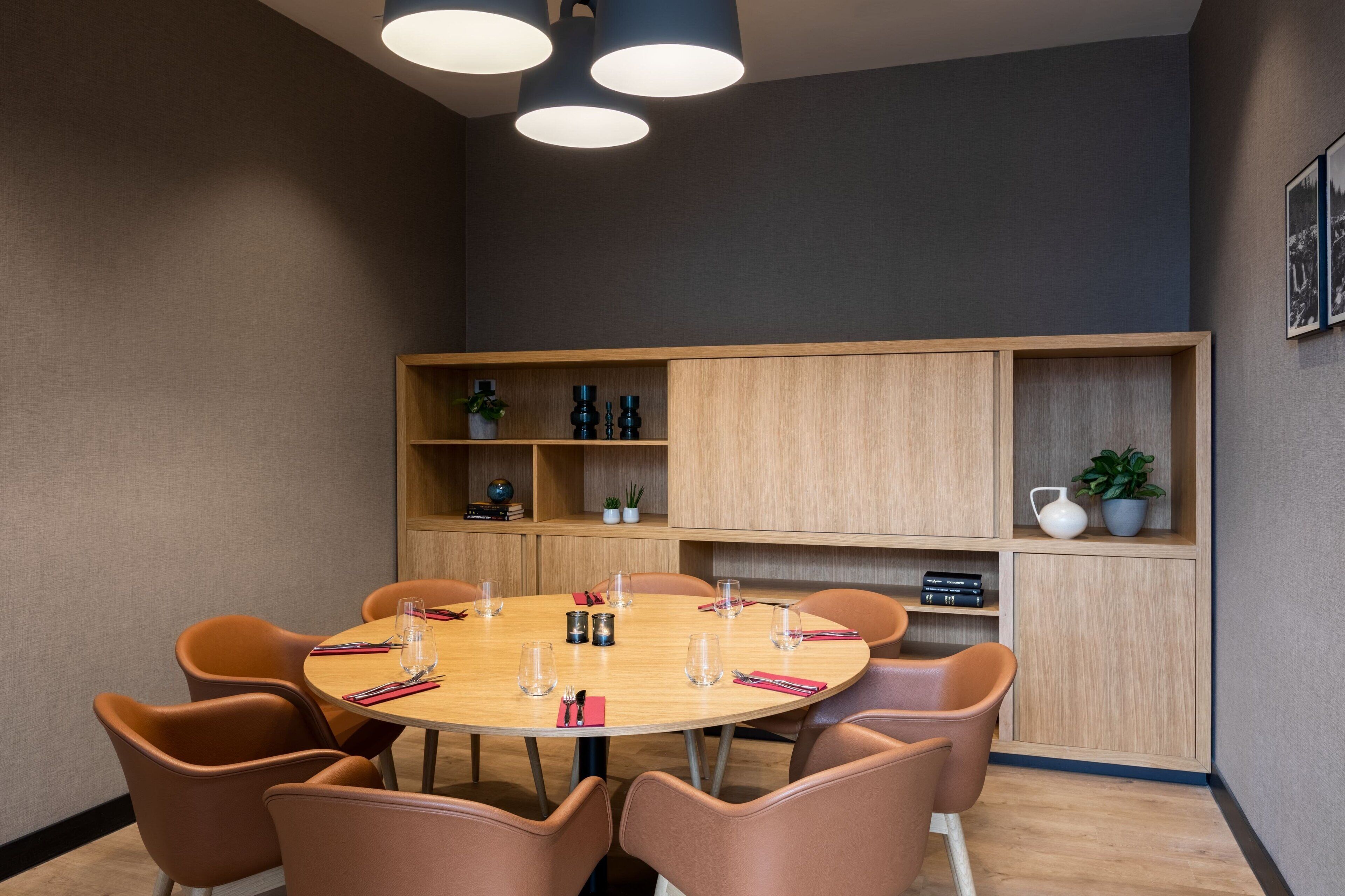 A conference room with a round table, six chairs, and a wooden cabinet with shelves.
