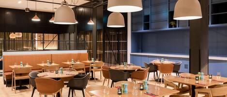 A modern restaurant interior with multiple dining tables and chairs, pendant lighting, and a bar area.