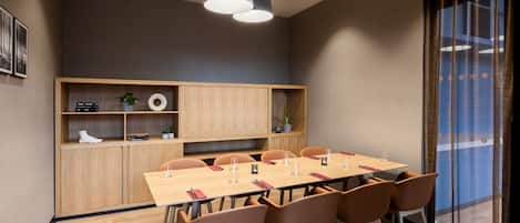 Una sala de reuniones moderna con una mesa larga, sillas marrones e iluminación colgante.