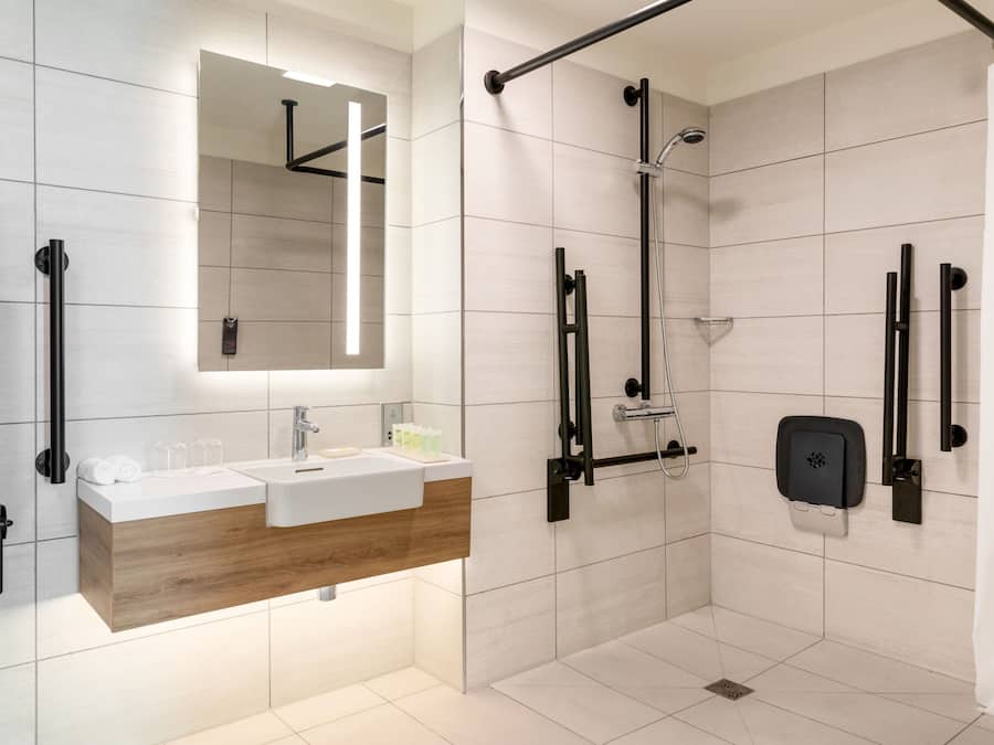 A modern bathroom with a wooden vanity, a large mirror, and a walk-in shower with grab bars.