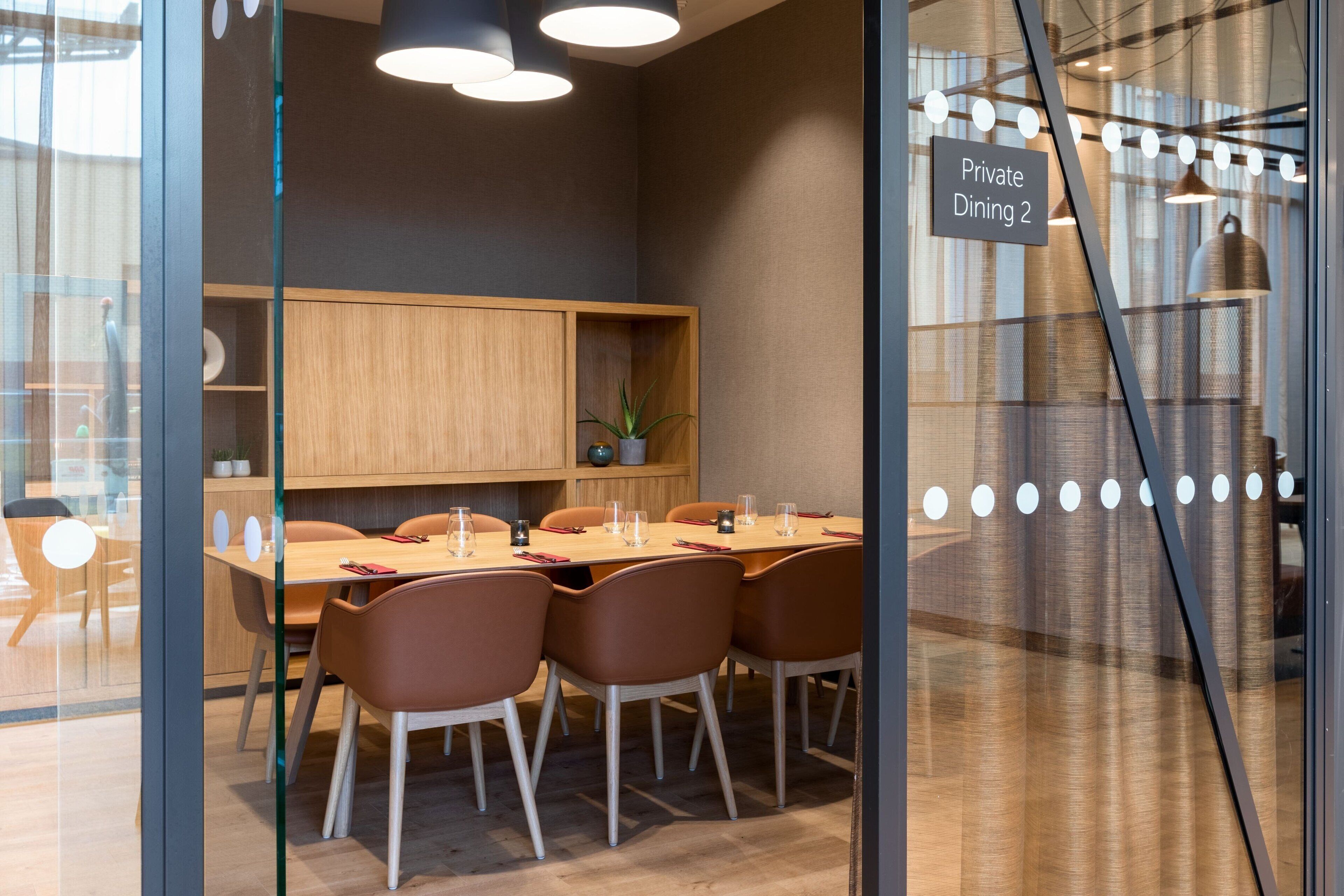 Uma área de refeições privativa com uma mesa de madeira, cadeiras marrons e uma placa com a inscrição 'Private Dining 2'.