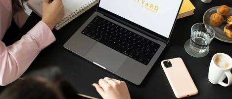 Una computadora portátil mostrando 'COURTYARD BY MARRIOTT' en la pantalla, un cuaderno, un teléfono inteligente y una mesa con pasteles y tazas de café.