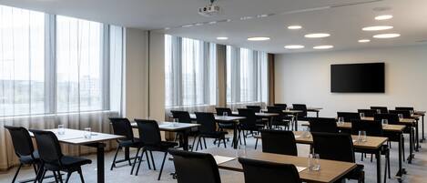 A conference room with tables and chairs, large windows, and a projector on the ceiling.