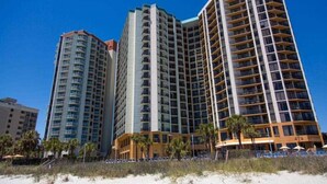 A high-rise hotel with multiple floors, a beach view, and a pool area with umbrellas. - 210Sea Gem. Oceanfront. Pet Friendly (Myrtle Beach)