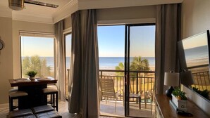A room with a wooden floor, a dining table with chairs, a sofa, a TV, and a balcony with a view of the beach. - 210Sea Gem. Oceanfront. Pet Friendly (Myrtle Beach)