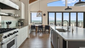 A modern kitchen with a large island, a dining area with a view of the ocean, and a large window overlooking the sea.