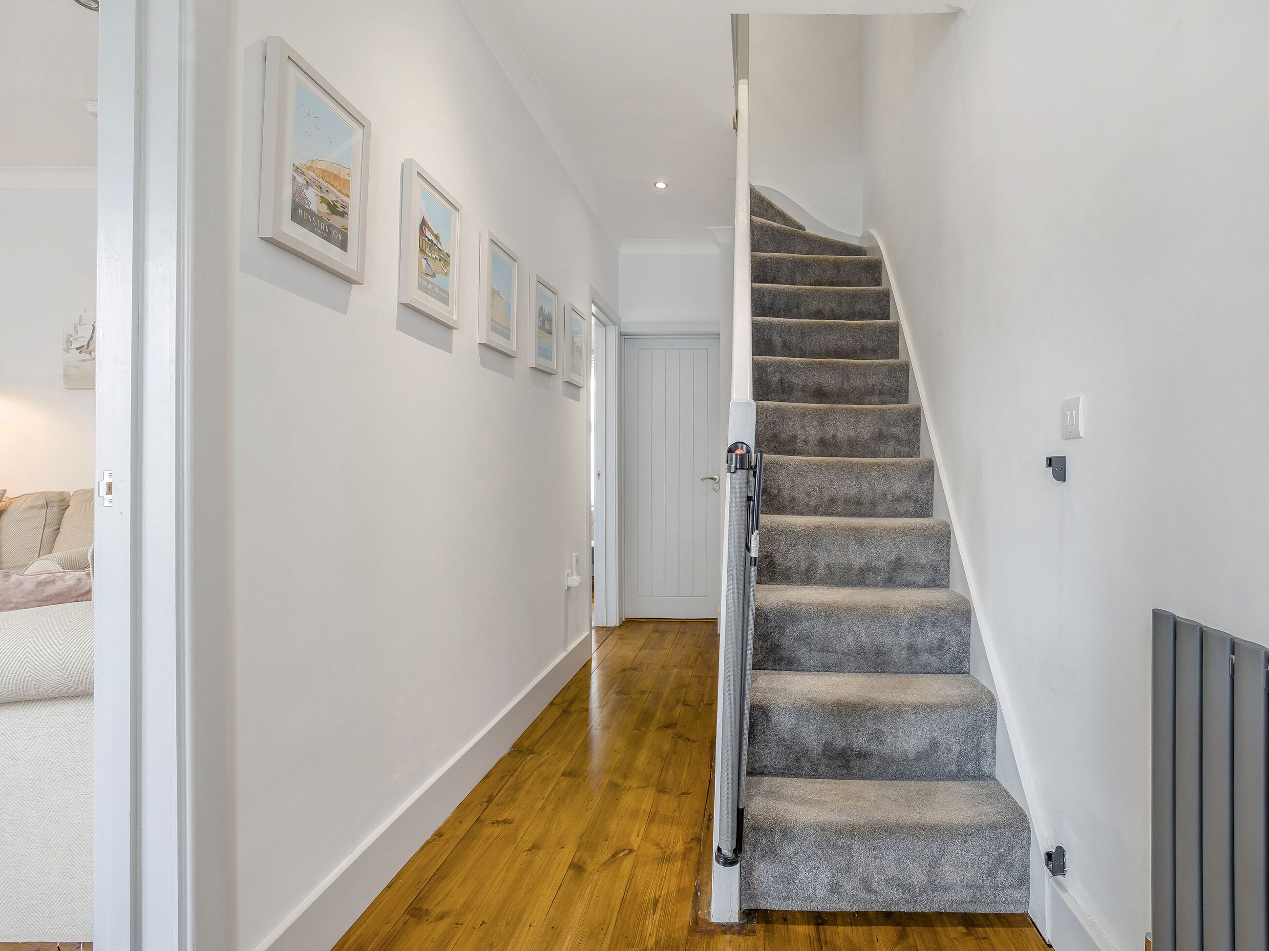 A staircase with carpeted steps, white walls, and framed pictures on the wall.