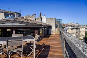 A rooftop terrace with a wooden deck, a table, and chairs, overlooking a cityscape. - Château Trompette (Bordeaux)