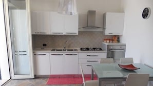 Een moderne keuken met witte kasten, een gasfornuis, en een eethoek met een glazen tafel en stoelen.