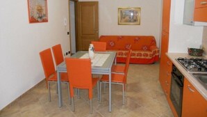 Een kleine keuken met een eettafel en stoelen, een bank en een fornuis.