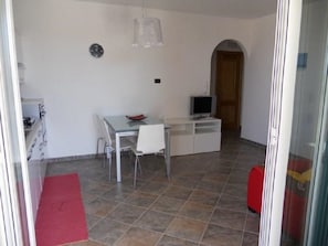 Un espace de vie compact comprenant un coin repas, un téléviseur et une valise rouge.