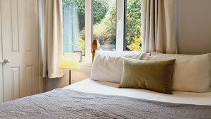 Een slaapkamer met een bed, een raam met gordijnen en een nachtkastje met een lamp.