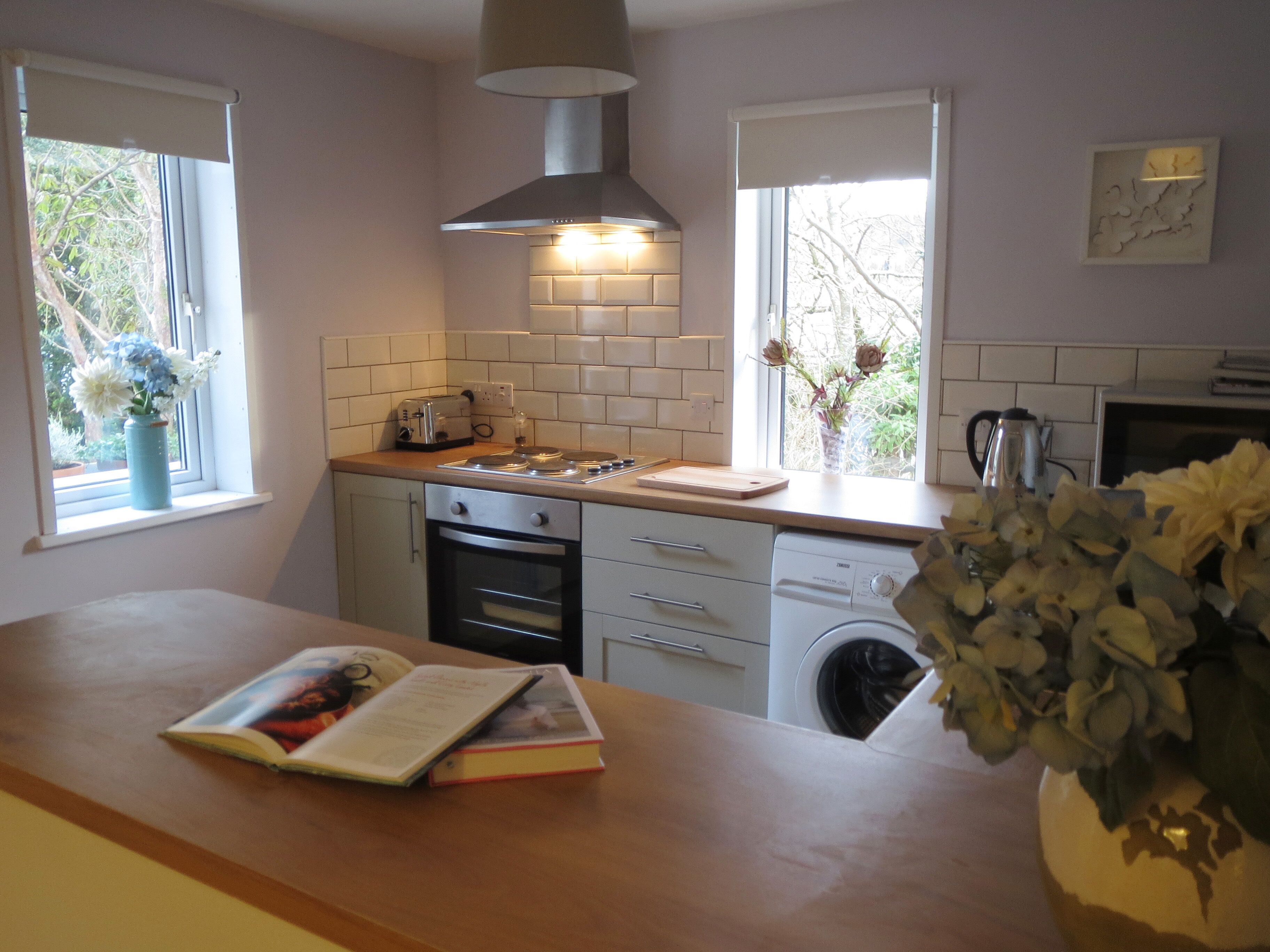 A modern kitchen with white cabinets, a built-in oven, a dishwasher, and a window with a view of greenery.