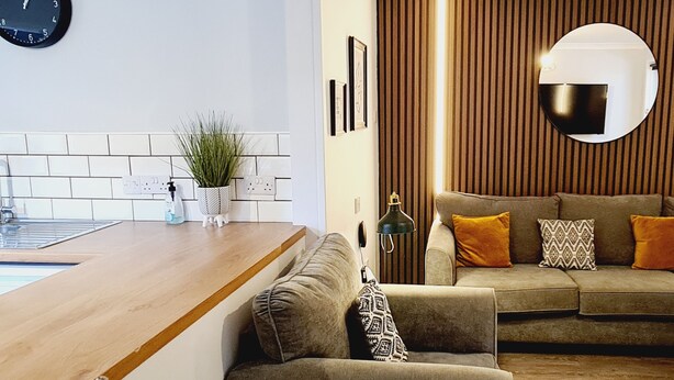Een moderne woonkamer met een houten salontafel, een bank met gestreepte kussens en een wandgemonteerde televisie.